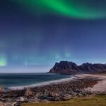 Beach Destinations - Body of Water Near Mountain Under Green Sky