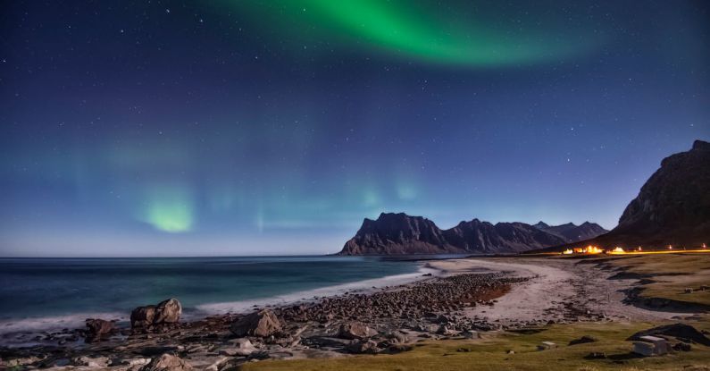 Beach Destinations - Body of Water Near Mountain Under Green Sky