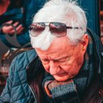 Dining Experience - Concentrated senior gray haired male in warm jacket sitting at table in outdoors cafe and holding glass