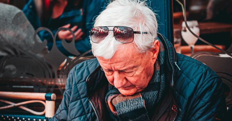 Dining Experience - Concentrated senior gray haired male in warm jacket sitting at table in outdoors cafe and holding glass