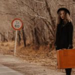 Hitchhike - Full body of female in elegant outfit and hat with old suitcase near leafless trees in autumn