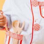 Culinary Experiences - Adorable African American child wearing uniform of cook standing with kitchen tools in studio