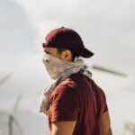 Sustainable Destinations - Unrecognizable man with scarf on face walking in sandy terrain terrain near windmills