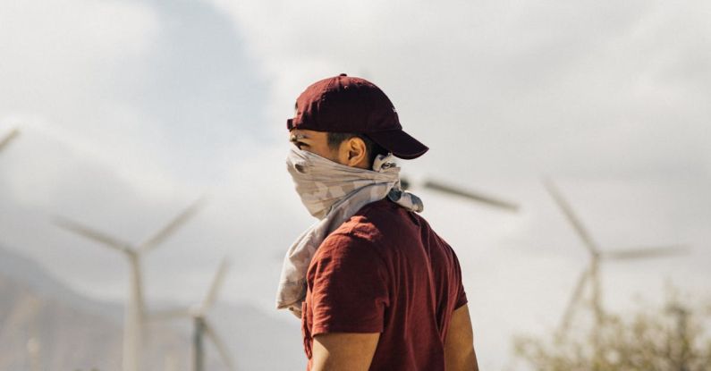 Sustainable Destinations - Unrecognizable man with scarf on face walking in sandy terrain terrain near windmills