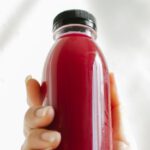 Detoxes - Unrecognizable woman holding bottle of red juice against white wall