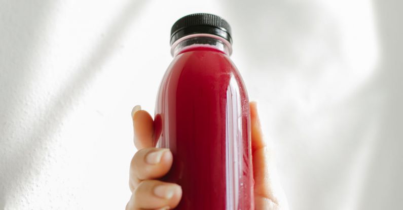 Detoxes - Unrecognizable woman holding bottle of red juice against white wall