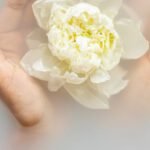 Rejuvenate - Unrecognizable female with soft manicured hands holding white flower with delicate petals in hands during spa procedures