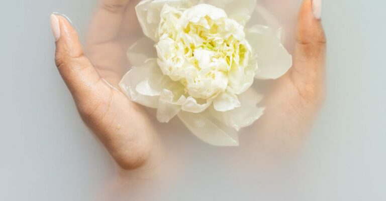 Rejuvenate - Unrecognizable female with soft manicured hands holding white flower with delicate petals in hands during spa procedures