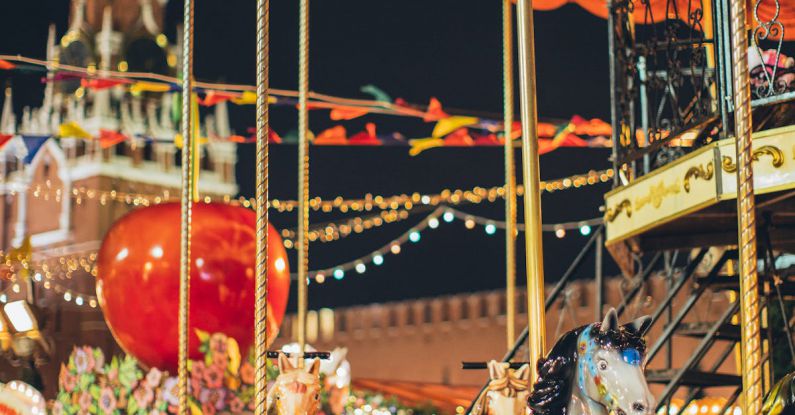 Theme Parks - Festive merry go round with carnival horses on Red Square against blurred Kremlin during New Year holidays in evening